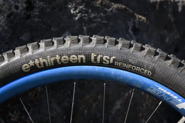 Joining e*thirteen’s ever-expanding product line-up last year, the e*thirteen TRSr is intended to slot in between lightweight cross-country tyres and super-burly downhill tyres – in the words of Goldilocks, not too hot and not too cold, but juuuust right. Or to put it another way, a regular trail tyre for everyday use. That might be doing these tyres a slight disservice though, as they’ve performed brilliantly throughout the test and are more than ‘just right’. Available in 27.5in and 29in options, with folding bead, reinforced sidewalls, reinforced pinch flat zones and enduro casing, they tip the scales at 918g (27.5in, 900g quoted) and are designed to pop up tubeless with just a track pump and a scoop of sealant. True to their word they went up without needing a compressor on every rim we tried, every time. Available in two compounds (Race or Plus), we’ve been riding the softer, grippier, Race compound which is made up of 70a rubber at the base, 42a in the centre, and a 40a for the side knobs. Given how soft the tyres feel under the thumbnail, they rolled along really well, and were only a bit draggy on long road sections. Once up to speed and onto the fun stuff though, that drag wasn’t noticeable, and the payoff was that they provided ample grip for climbing, especially when faced with things like slanted wet rock or rooty madness sections. If outright climbing traction isn’t required, you might want to consider either the harder compound TRS+, or a modern semi-slick such as the Maxxis Minion SS. The sidewalls felt really supportive and I often found myself running less pressure than I thought – sometimes as low as 22/24 psi front/rear, with very little tyre body roll, while on rockier Lakeland descents we upped the pressures slightly. Even if you go fast enough to drift, the traction is super-reliable except on very loose marbley surfaces, where we have yet to find a tyre that works perfectly. With a carefully shaped and siped tread pattern reminiscent of a Magic Mary, they offer great grip in mud and slop too, with lots of clearance, and the rubber was soft and edgy enough to keep things under control for braking when the going got loose. On the first off-road descent of the first ride on the tyre, we managed to put a hole in the rear that needed two tubeless plugs to seal. However, after that, it has been puncture and trouble free for over a year, even hitting long rocky Lakeland descents where we could feel the tyres bottoming out and carbon rims impacting on the ground below. As such, the pair of tyres on test has done a hard week of descending in the Pyrenees, many rides around Calderdale, trips to Peebles, and finally they’ve ended up here in the Lakes. They’ve not been ridden every day as they’ve been on a ‘weekends and trips’ bike, but we reckon they’ve done a good few hundred miles. While the rear is worn, they are looking surprisingly good for their age, and for the amount of riding time we’ve put into them in relation to the level of grip they return, the wear has been excellent and as they’ve worn the performance hasn’t fallen away as dramatically as it has with other tyres on test. Overall There is no denying that at £59.95, they’re at the upper-mid end of the price spectrum, but we’ve really got on well with these tyres, If you think of them as track day tyres for your sports car, it’s well worth getting a pair for racing and Alps trips and maybe use something else for day-to-day riding.
