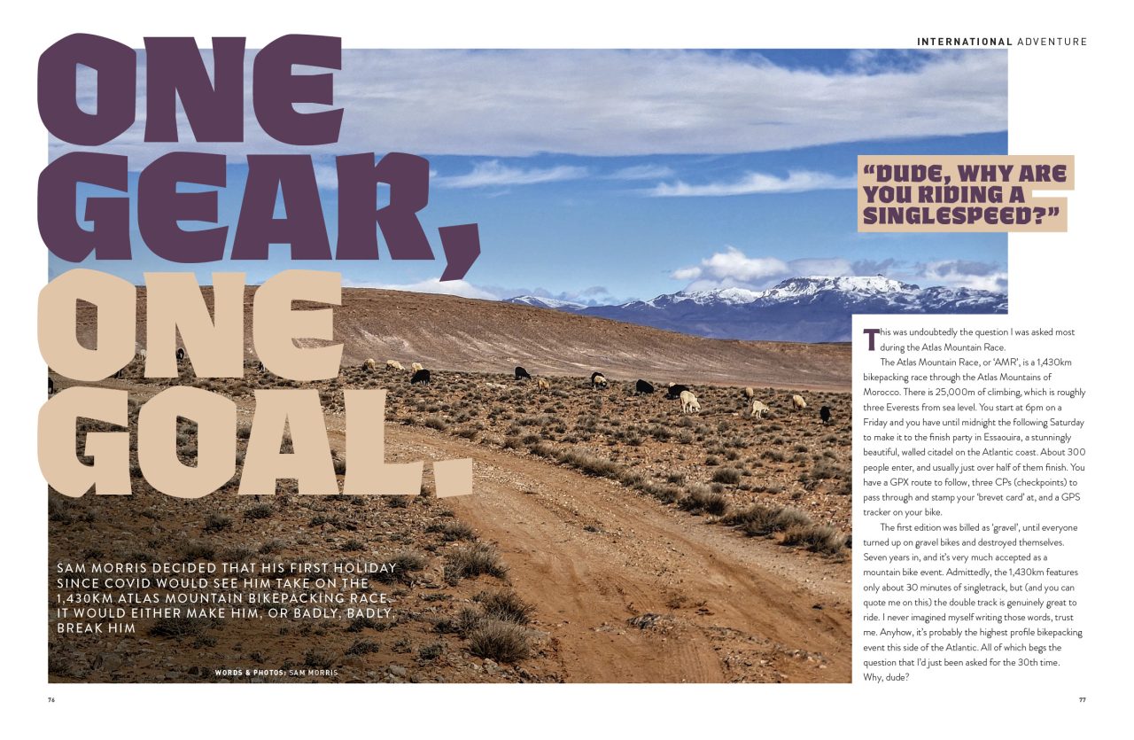 A scenic landscape featuring a dirt road winding through barren terrain with grazing sheep, set against a backdrop of mountains under a blue sky. Bold text overlays read: 'ONE GEAR, ONE GOAL' and a quote asking, 'Dude, why are you riding a singlespeed?'