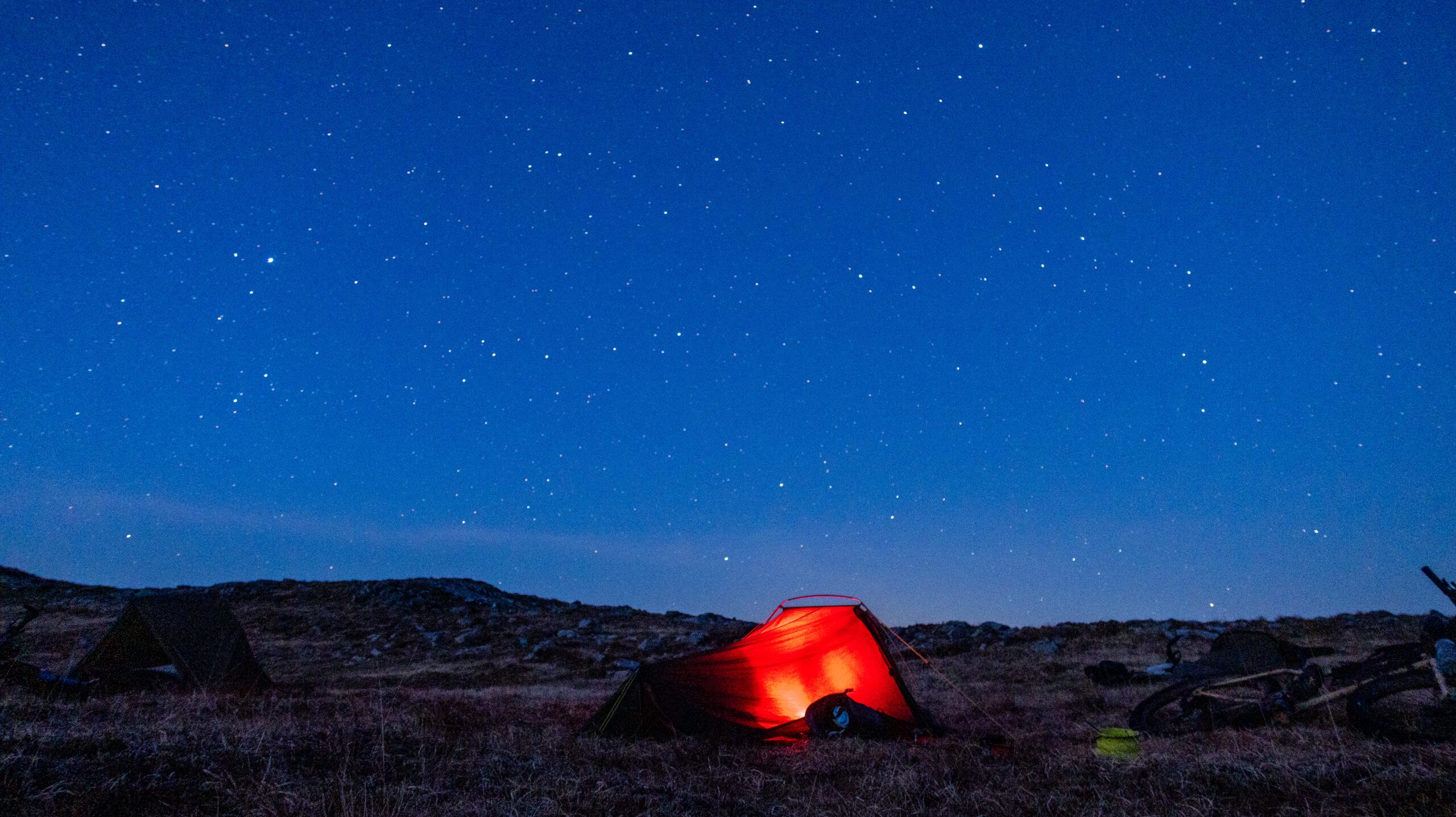 A glowing red tent in a field under a starry night sky.