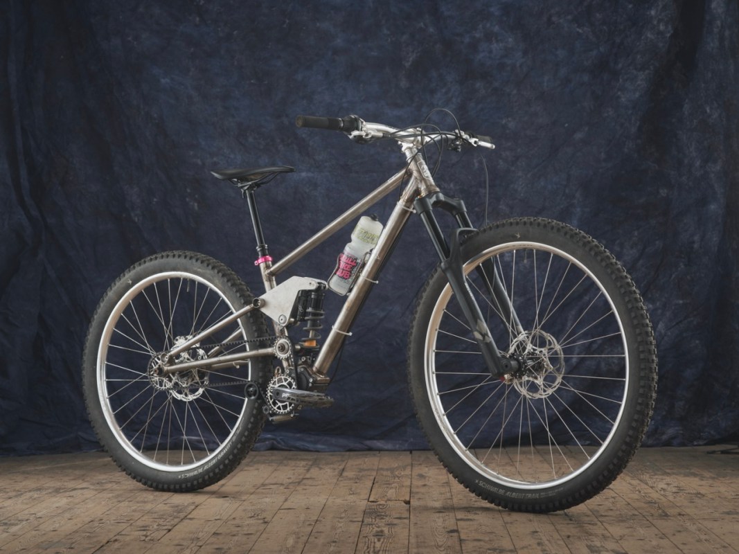 A custom-built mountain bike featuring a full suspension system, a pinion gearbox, and a unique design with adjustable components for enhanced performance and adaptability.