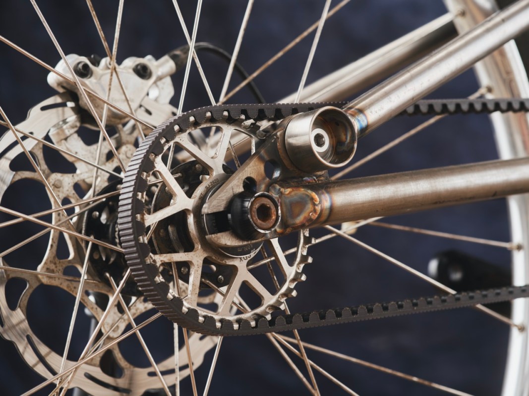 Close-up of a bicycle's rear suspension and gearbox system, showcasing a belt drive and disc brake components.