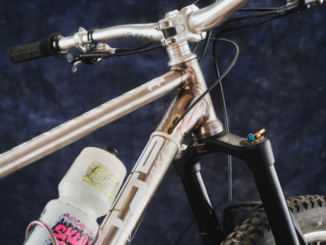 Close-up of a custom bike frame showcasing the handlebars, head tube, and a water bottle, with a blurred background.