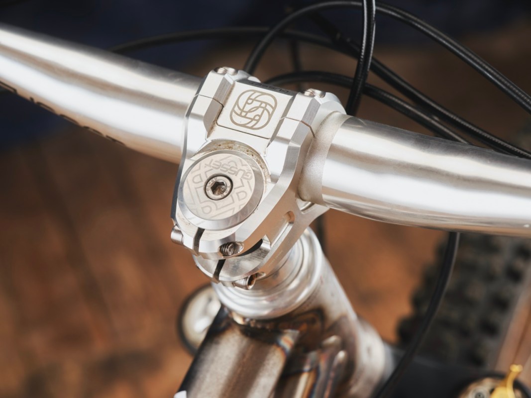 Close-up view of a mountain bike's handlebar and stem, featuring metallic components and cables.