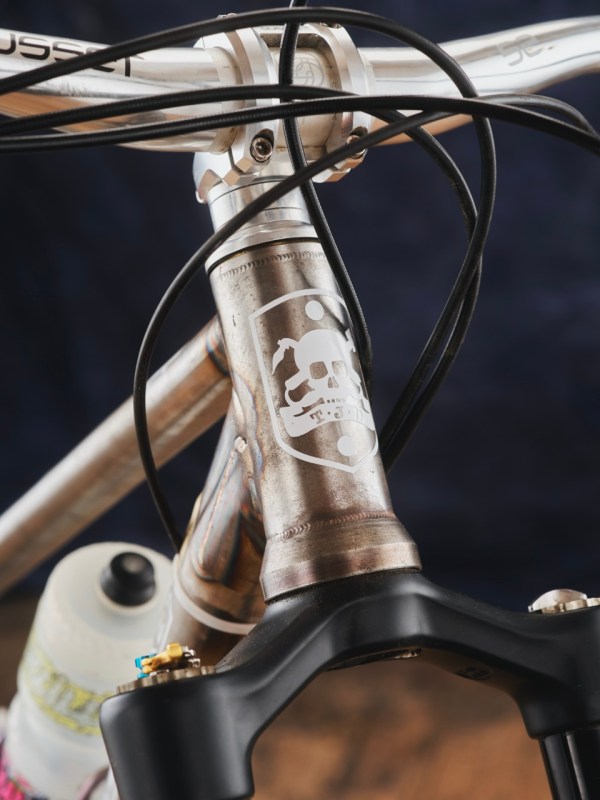 Close-up view of a bicycle's head tube with a skull logo, showcasing welding details and cable routing.