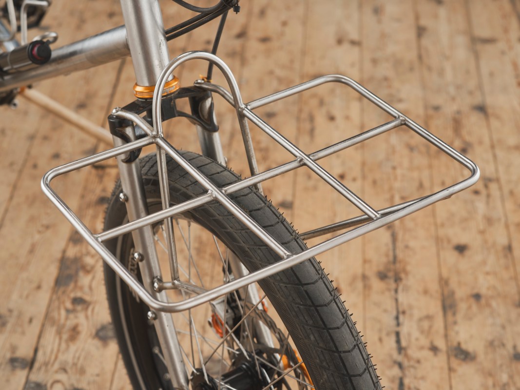 Close-up view of a front bike rack attached to a mountain bike, showcasing the tire and metal frame, with a wooden floor in the background.