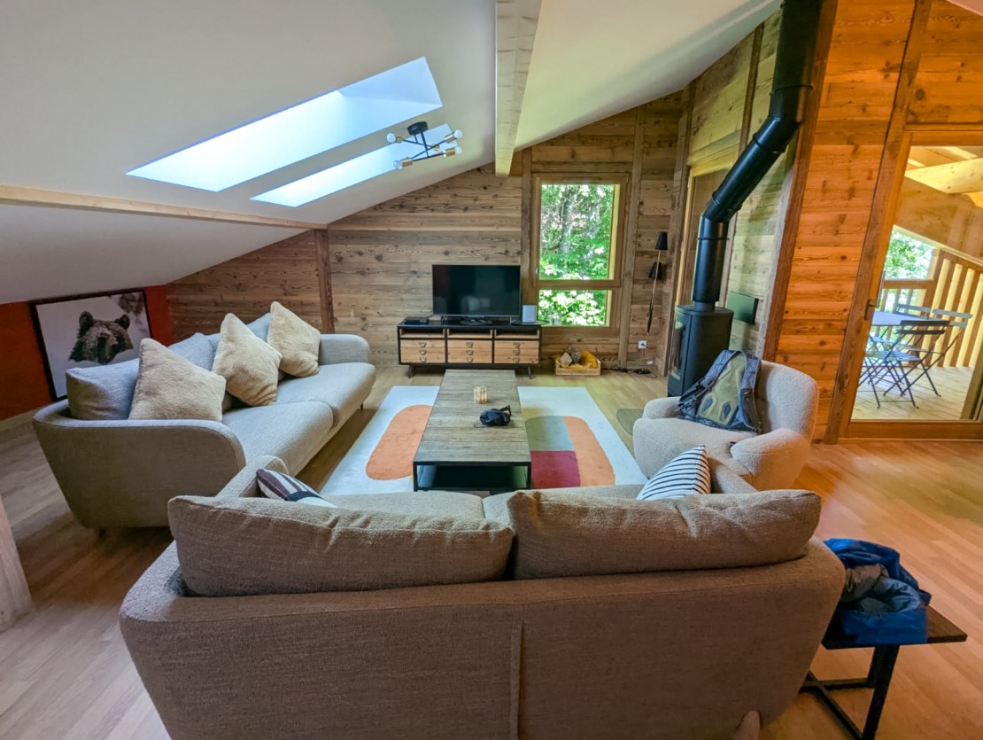 Cozy living room in a wooden chalet with large windows, a television, and comfortable seating.