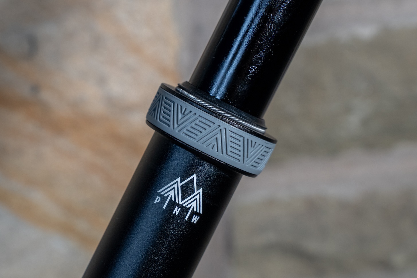 Close-up of a black bike seat post featuring a patterned grey ring and a white logo.