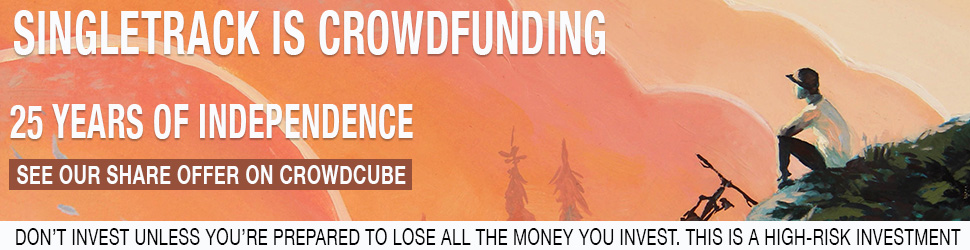 A person sitting on a rock, observing a colorful sunset over a mountain landscape, with a bicycle nearby.