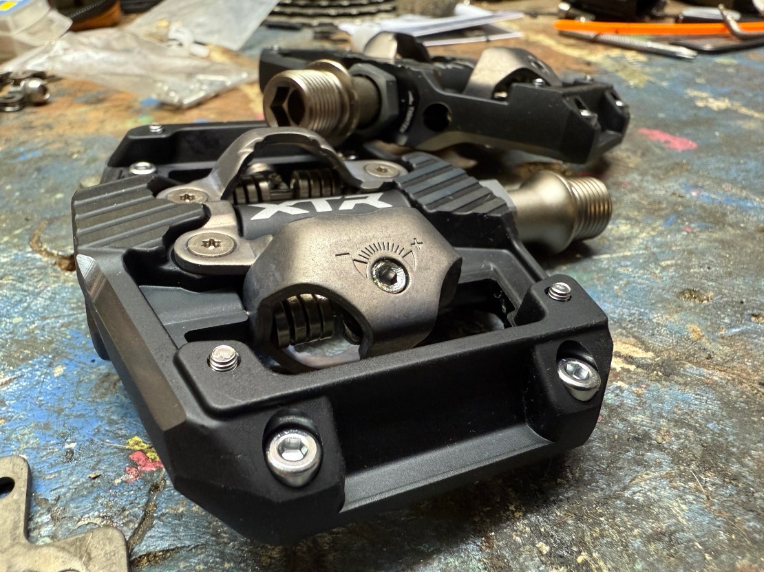 Close-up of Shimano XTR trail pedals on a workbench, showcasing the pedal mechanism and platform design.