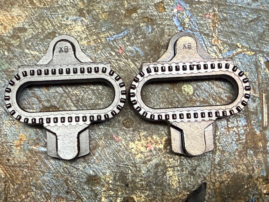 Close-up view of two Shimano XTR cleats on a textured surface, highlighting their metallic finish and design features.