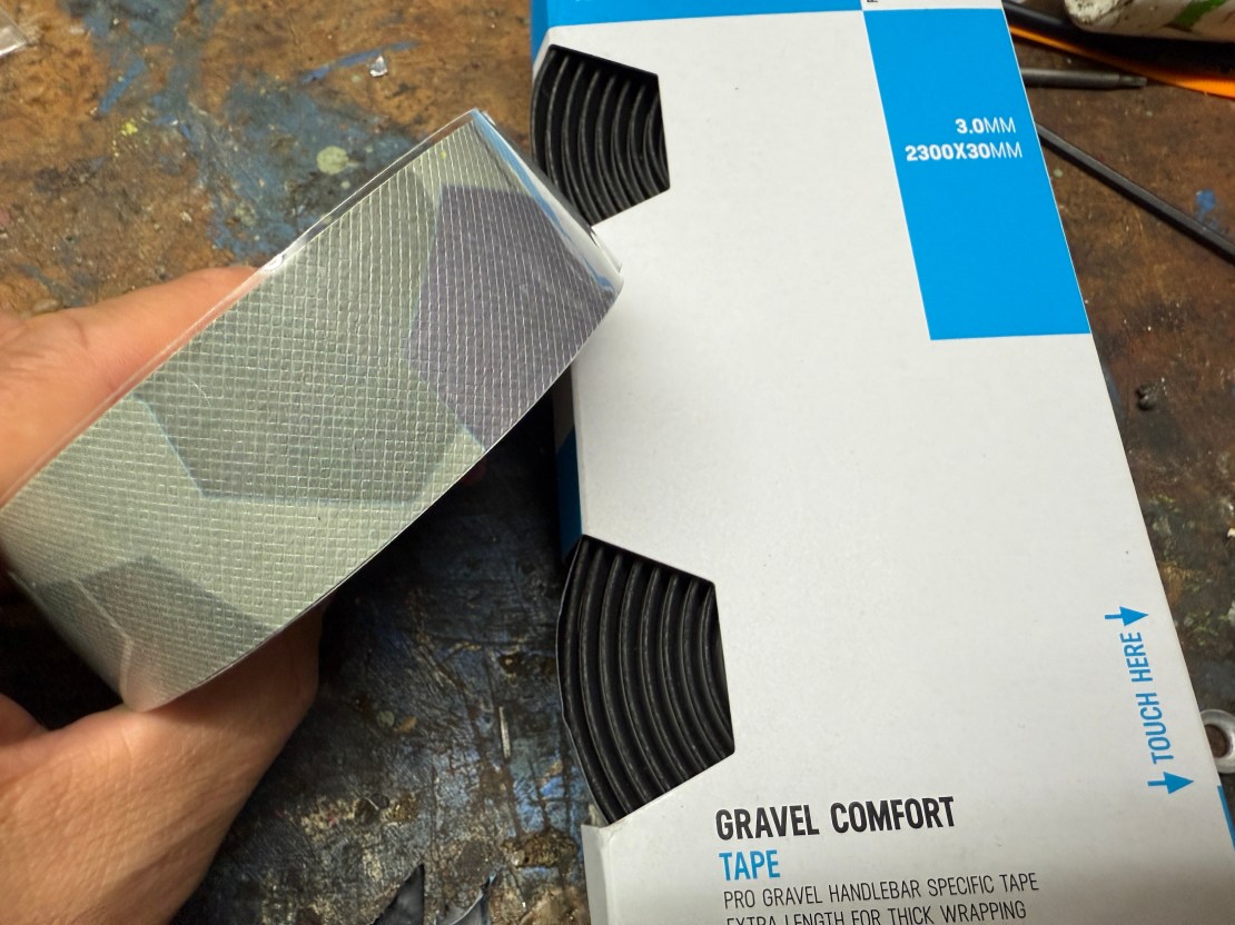 A hand holding a roll of Pro Gravel Comfort Tape next to its packaging, which details the specifications and features of the product.