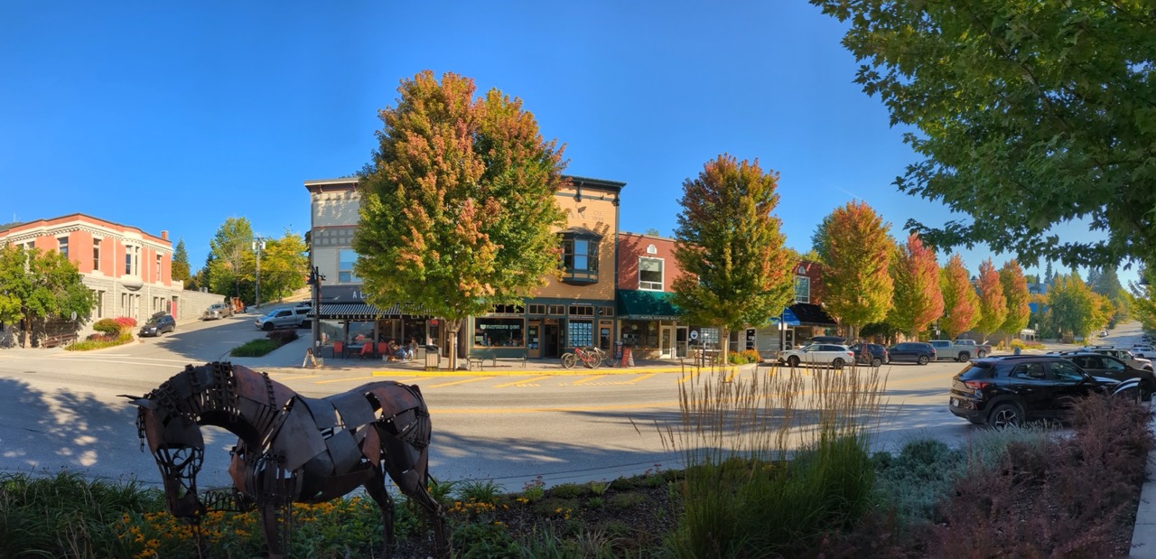 A panoramic view of downtown Rossland, Canada, showcasing colorful autumn trees, historic buildings, and a sculpture of a horse in the foreground.