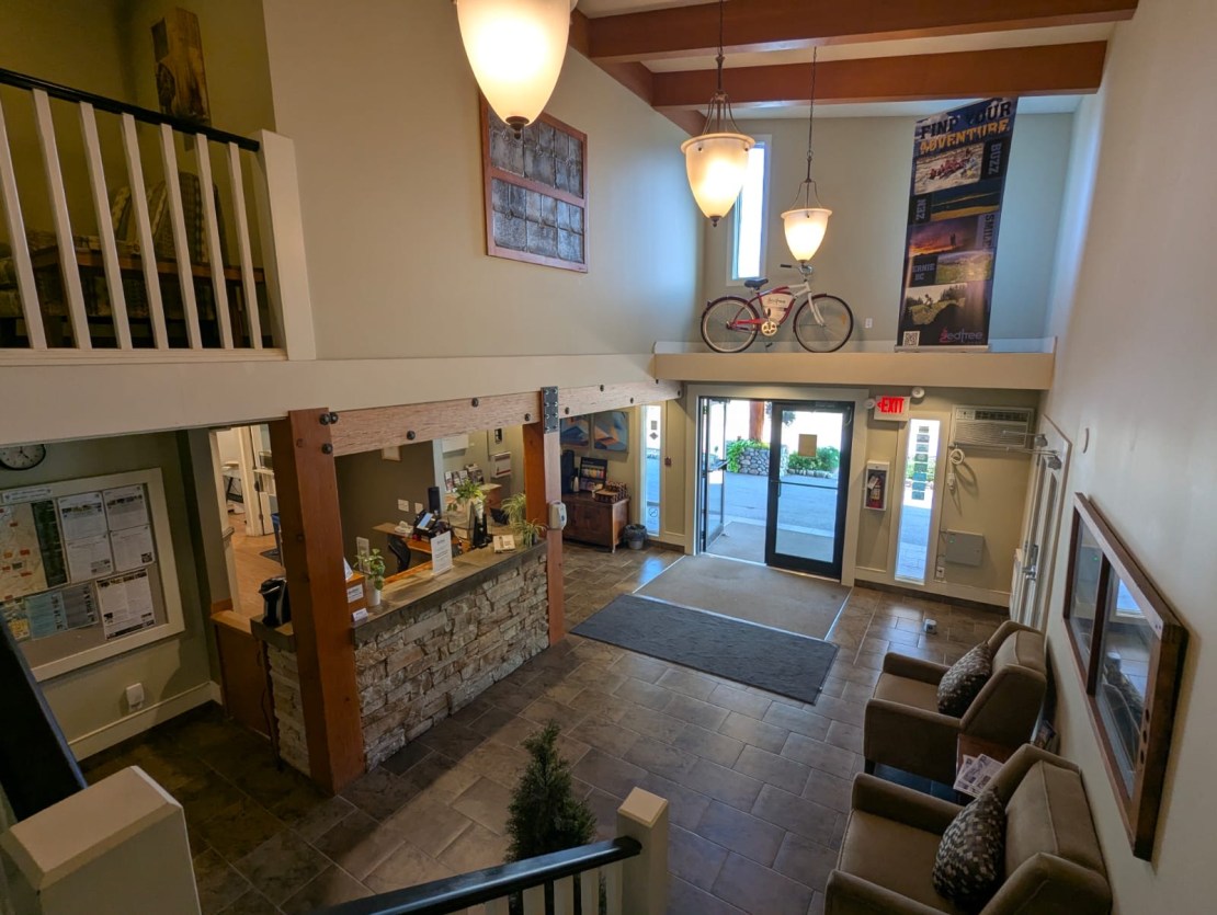 Interior view of a red tree lodge lobby in Fernie, Canada, featuring a reception area, seating arrangements, wooden beams, and a bicycle hanging on the wall.