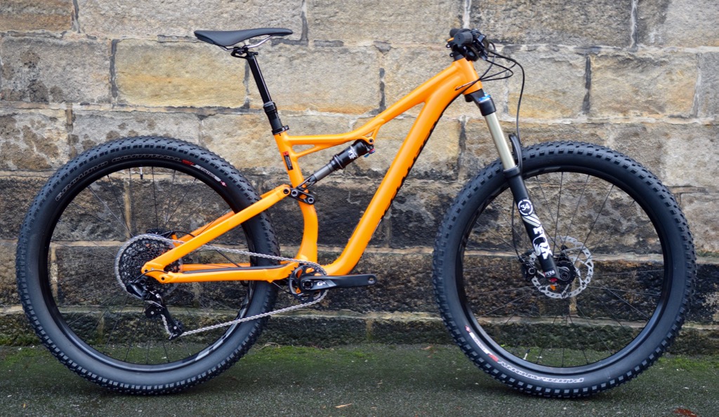 Side view of an orange Specialized Stumpjumper FSR mountain bike with fat tires, set against a stone wall.