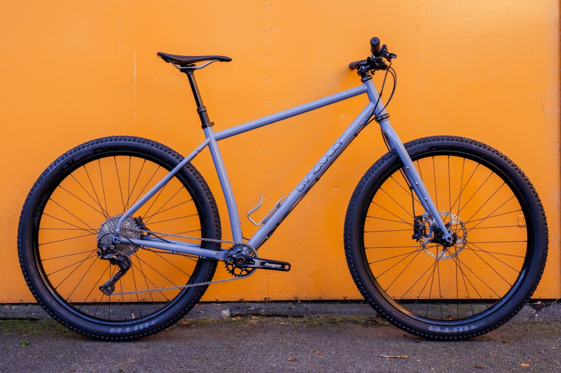 A gray gravel bike from Singular Cycles with wide tires, mounted on a background of solid orange color.