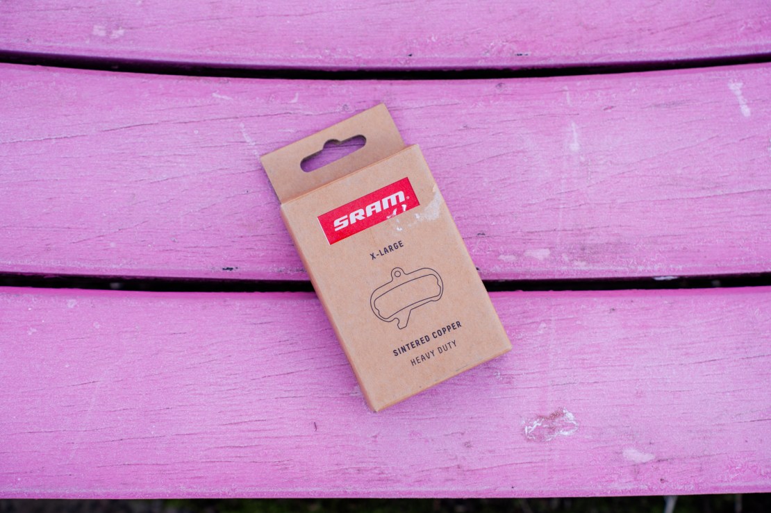 A SRAM X-Large sintered copper heavy-duty disc brake pad package on a pink wooden surface.