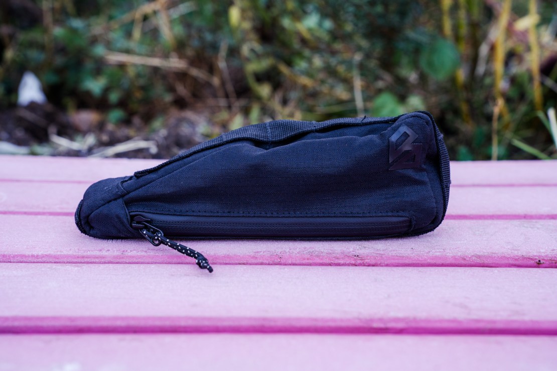 A black frame pouch mounted on a pink wooden surface, designed for bicycle storage.