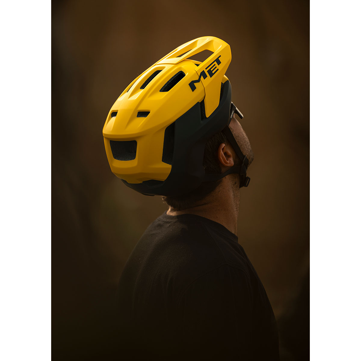 Close-up of a person wearing a MET Terrae MIPS helmet, featuring a yellow and black color scheme, against a blurred background.