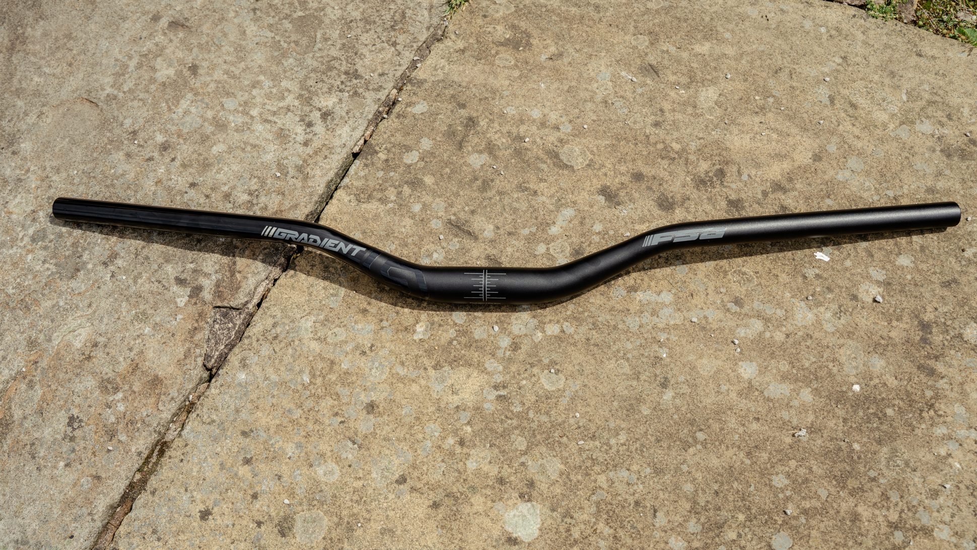 A Gradient handlebar lying flat on a textured surface, showcasing its black finish and branding.