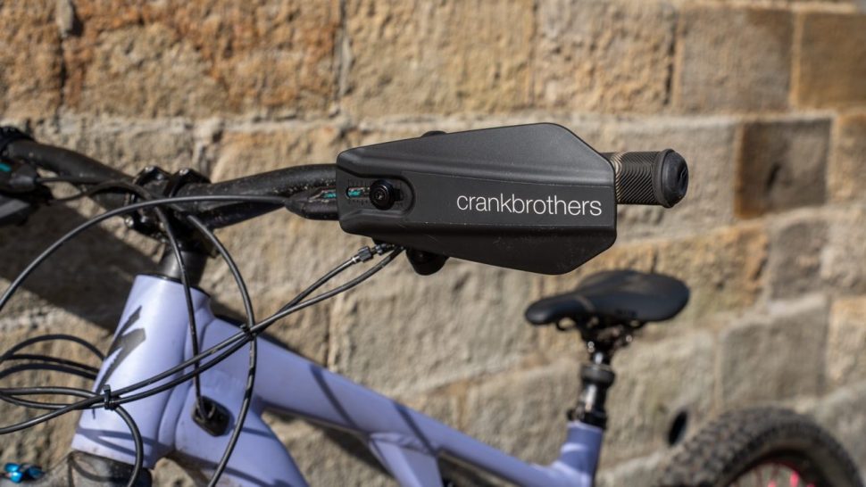 Close-up of Crankbrothers handguards mounted on a mountain bike handlebar, showcasing their design and features against a textured stone wall.