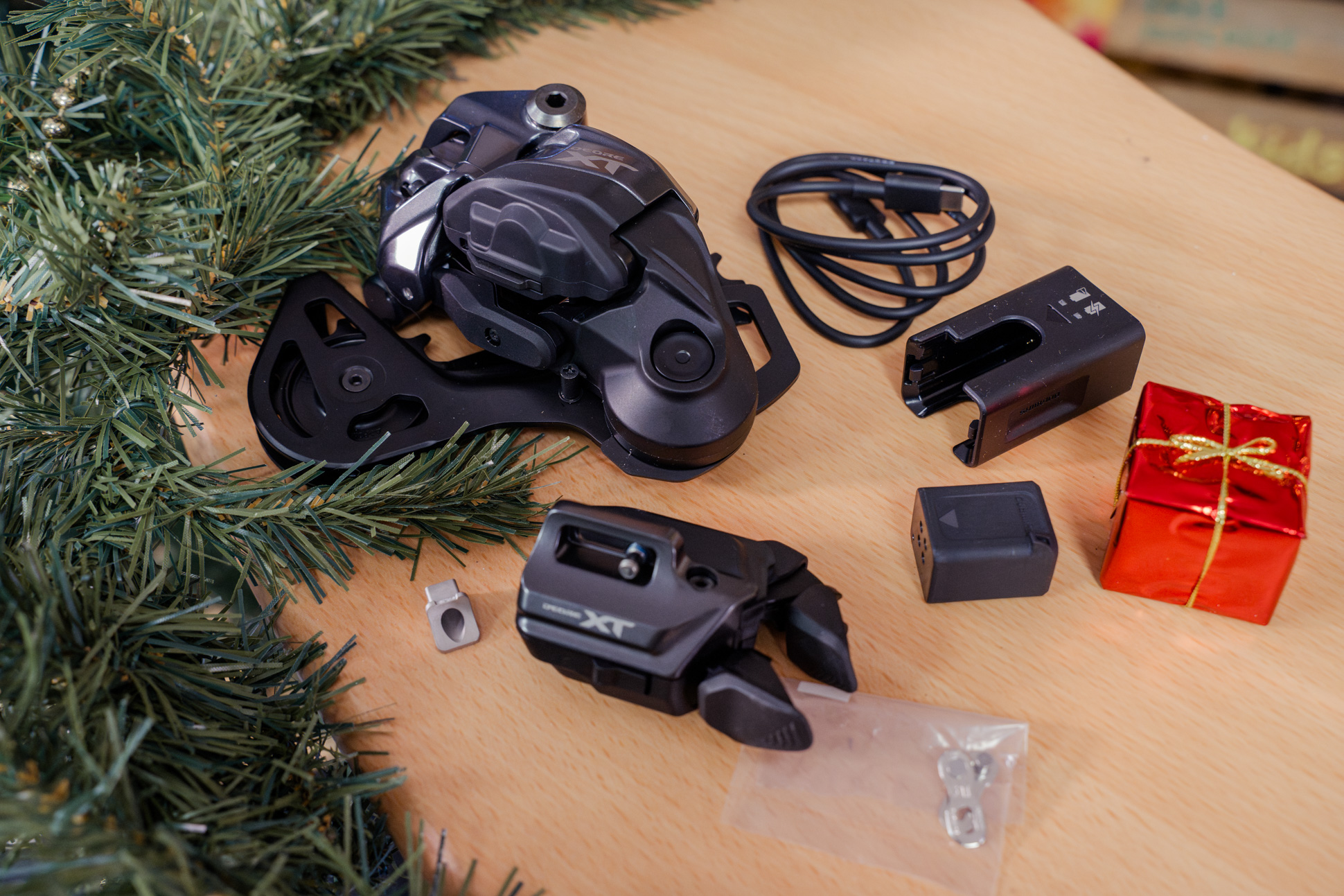 Shimano XT Di2 bike upgrade kit displayed on wooden surface, including rear derailleur, shifter, battery, charger, and a small gift box.