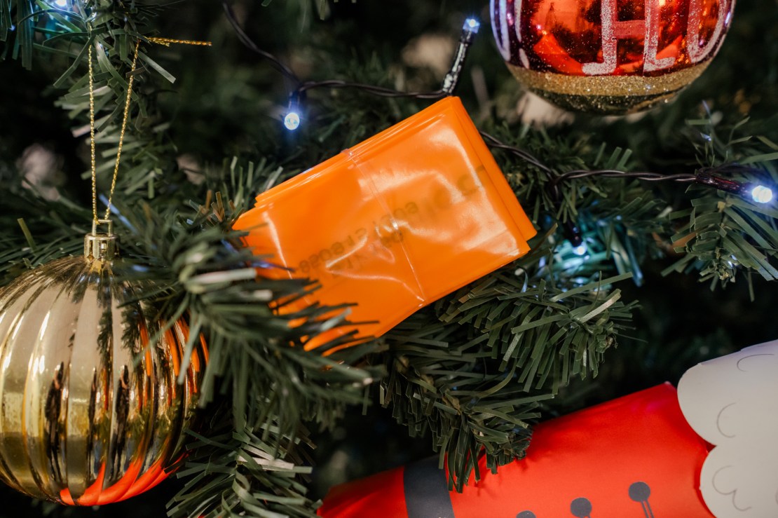 An orange Tubolito techno tube hanging on a Christmas tree alongside gold ornaments and colorful decorations.