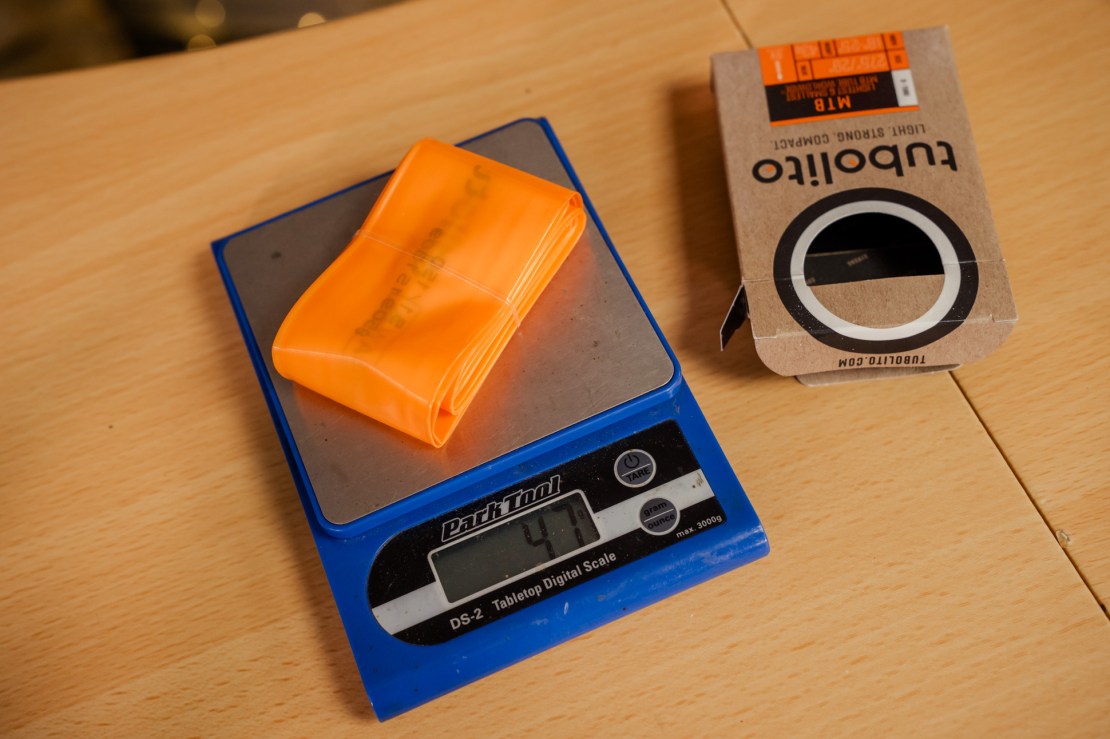 A lightweight Tubolito techno tube in bright orange on a digital scale reading 47 grams, next to its packaging.