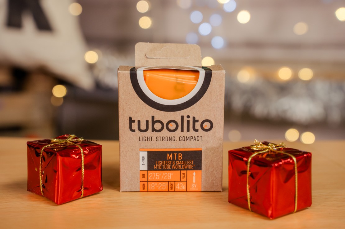 A Tubolito MTB tube package, prominently featuring an orange tube, sits on a wooden surface next to two small red gift boxes, with a blurred festive background.
