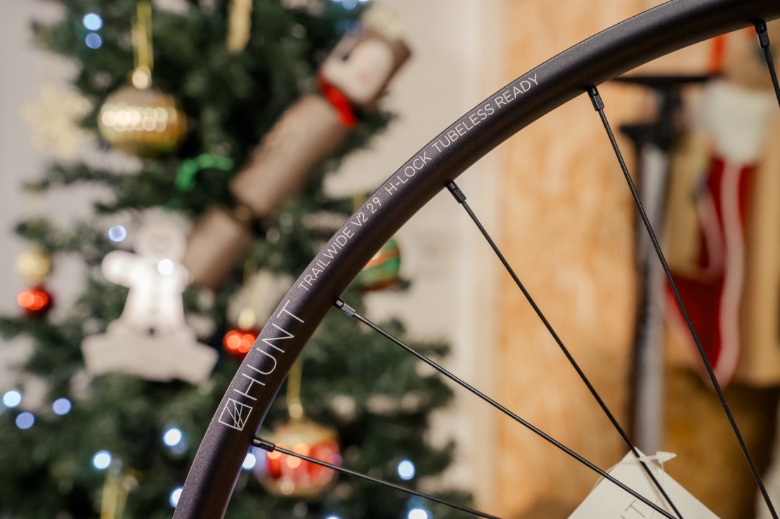 Close-up of a HUNT Trail Wide V2 29 wheel, showcasing its design details and 'H-LOCK TUBELESS READY' engraving, with a decorated Christmas tree in the background.