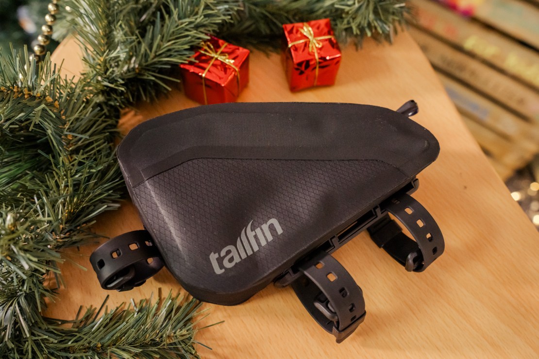 A black bike accessory bag from Tallfin, displayed on a wooden surface with decorative Christmas gifts and greenery.