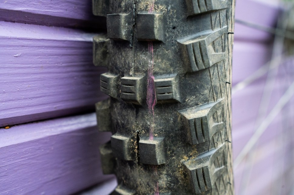 Close-up of a mountain bike tire showing the tread pattern and wear, against a purple wooden surface. Schwalbe magic mary radial