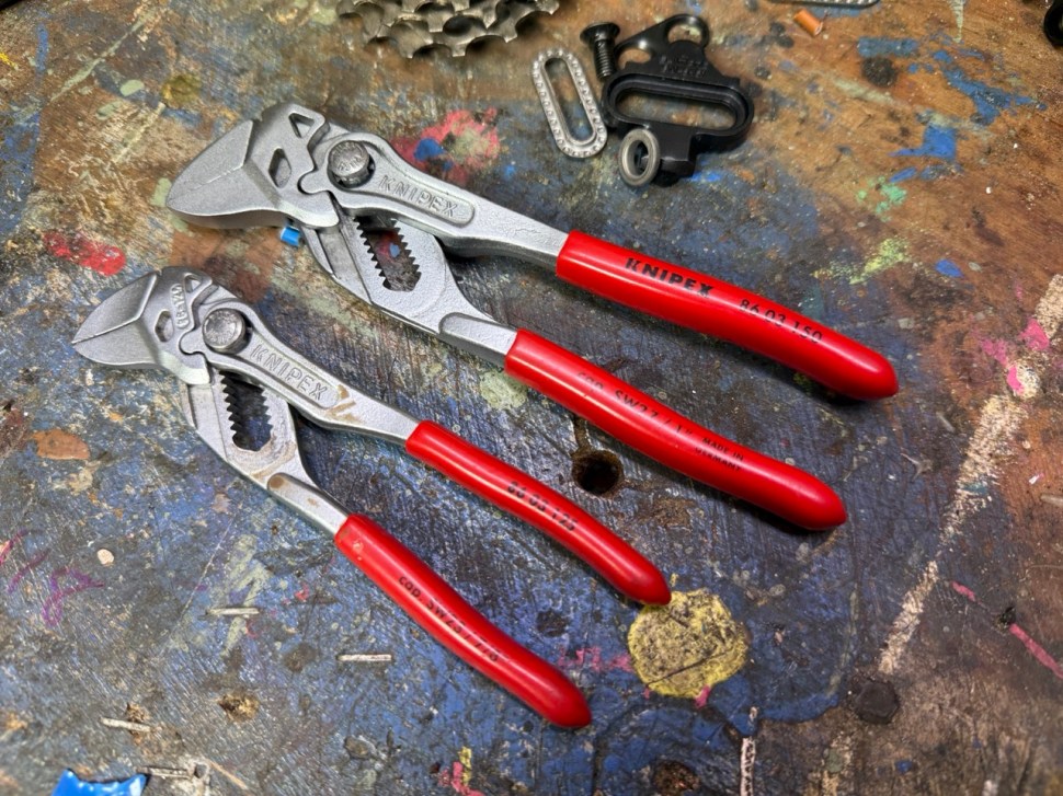 Two Knipex adjustable pliers with red grips resting on a colorful workbench cluttered with tools and bike parts.