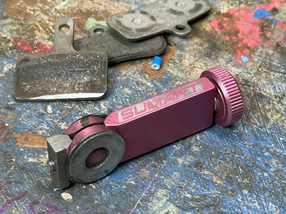 A pink Sumart UBB-20 brake tool on a blue and textured work surface, alongside a used brake pad.