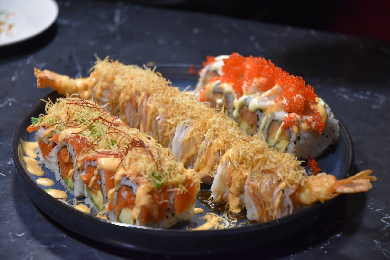 A plate of sushi featuring a variety of rolls, including shrimp tempura and colorful toppings, served with a dark background.