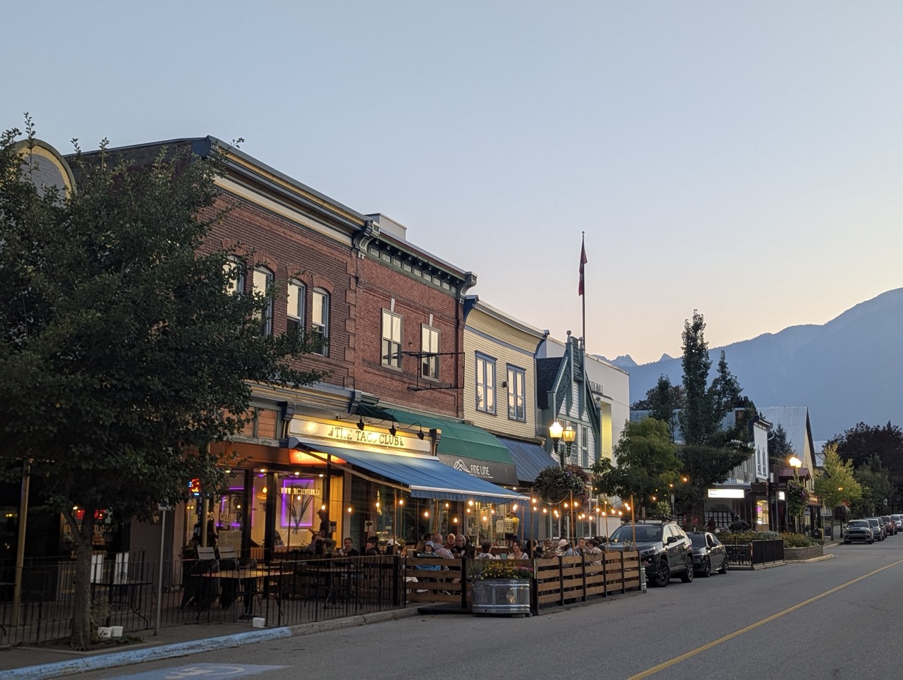 Street view of downtown Revelstoke, Canada, featuring The Taco Club restaurant and surrounding buildings amidst a mountain backdrop at dusk.