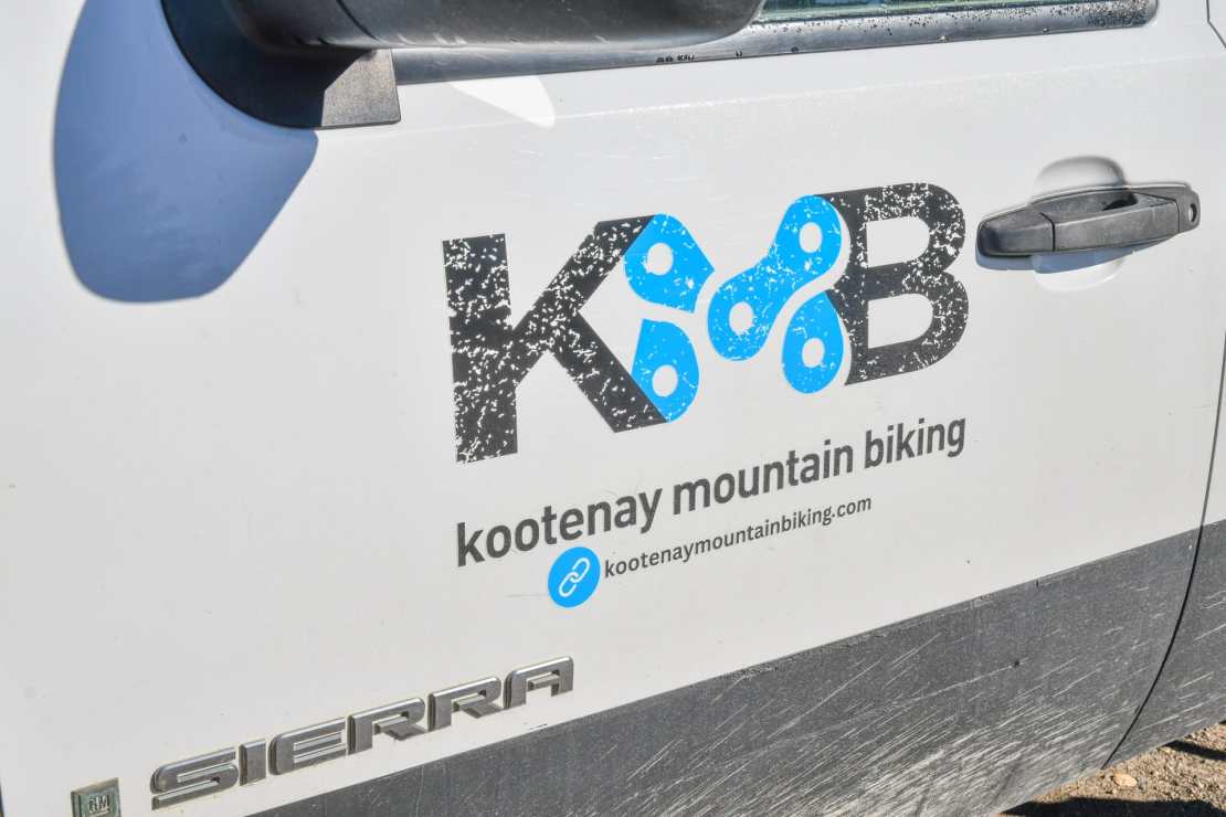Detail of a vehicle door with the logo of Kootenay Mountain Biking, featuring a bicycle chain graphic and the website URL.