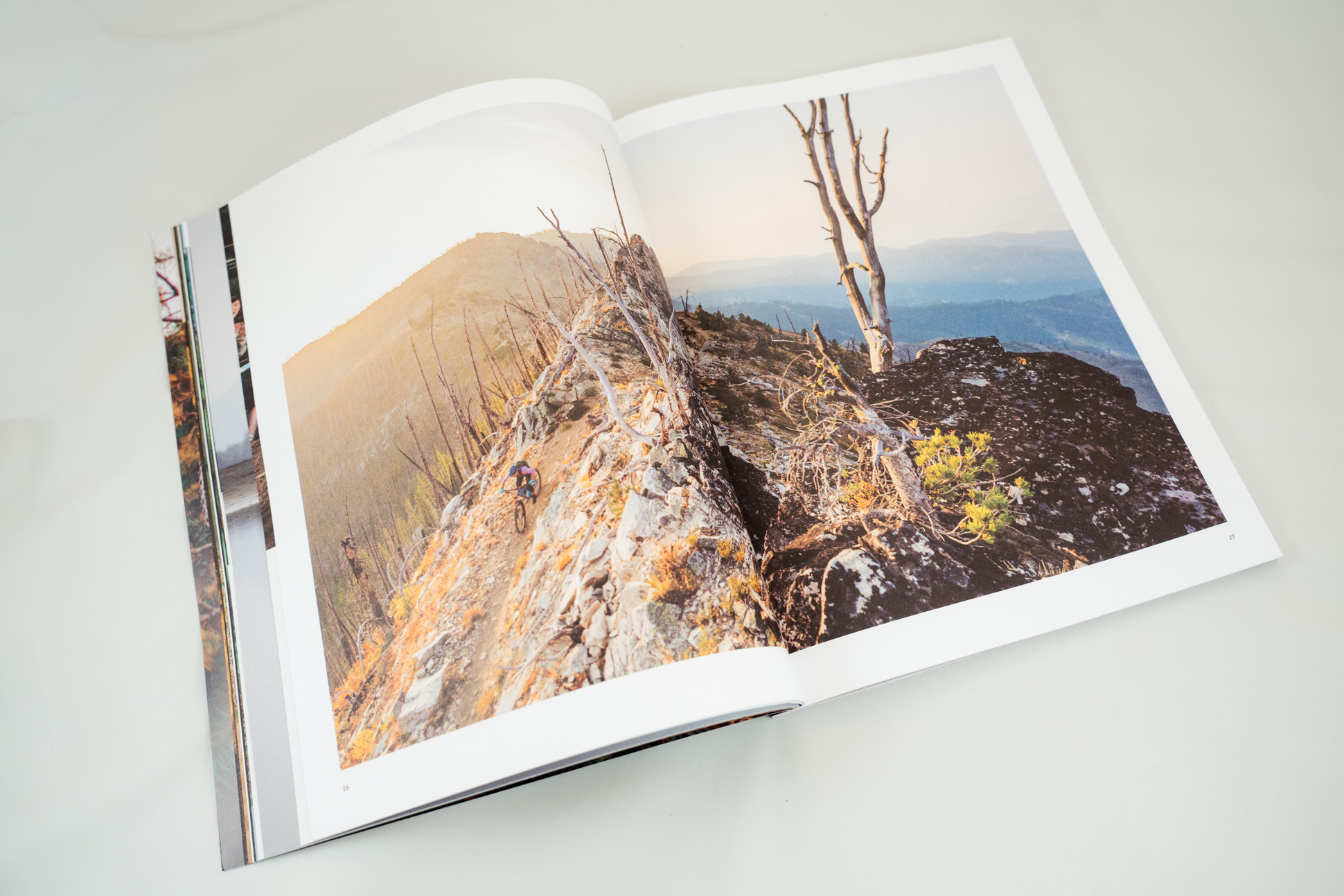 An open book displaying a landscape photograph showcasing a rocky mountain trail at sunrise with a cyclist navigating the terrain.