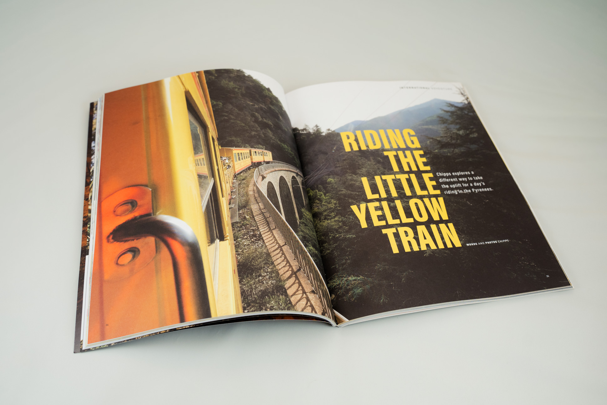 An open magazine featuring an article titled 'Riding the Little Yellow Train' with a photograph of a yellow train travelling through mountainous terrain.