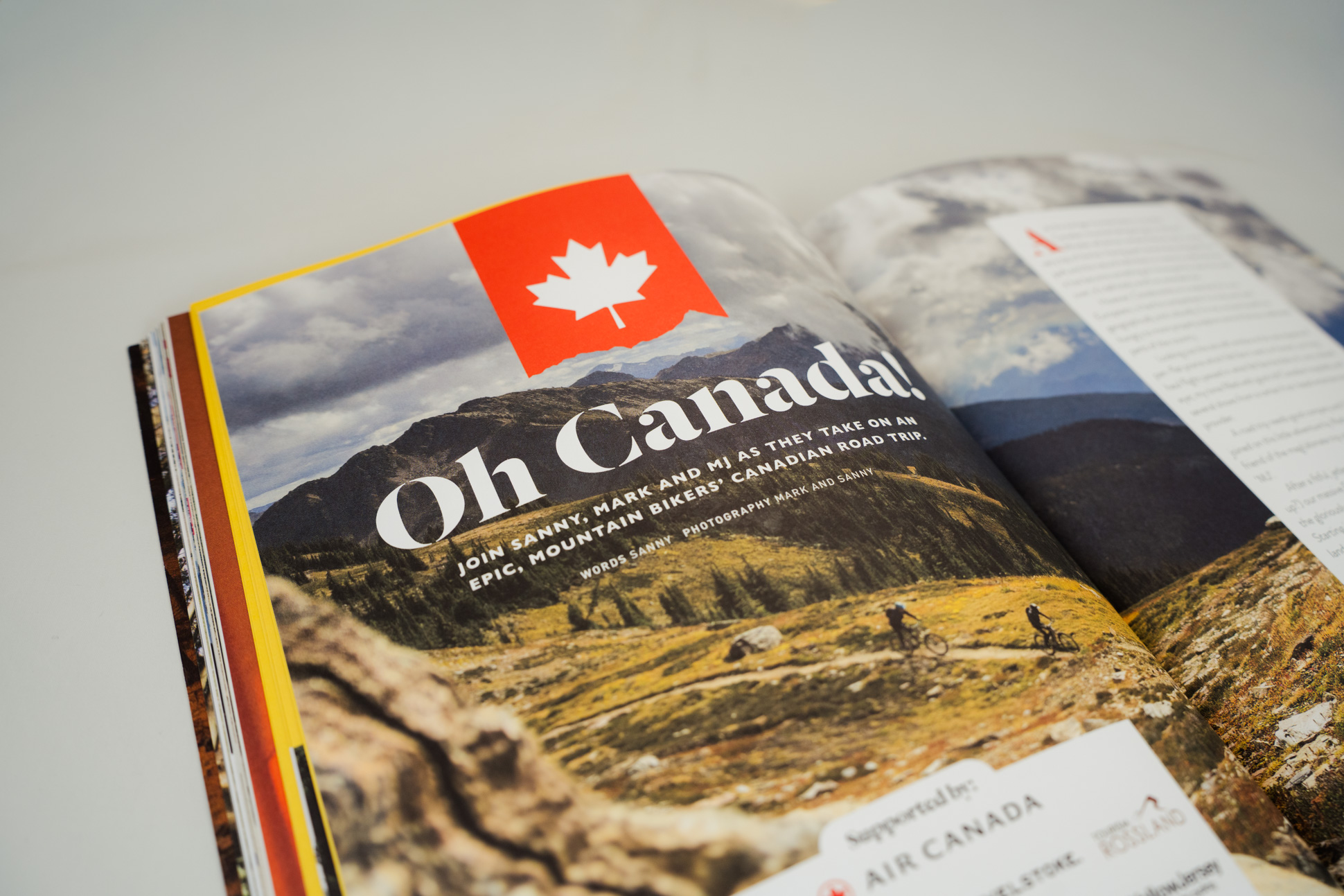 A magazine spread featuring the title 'Oh Canada!' with a Canadian flag graphic, promoting an epic mountain biking road trip. The image shows scenic mountain landscapes and cyclists on a trail.
