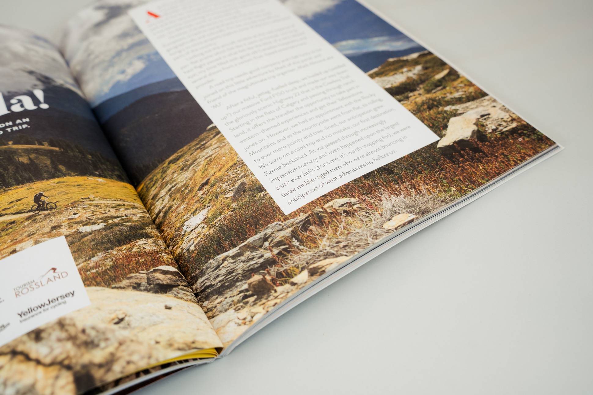 A close-up view of an open magazine featuring a scenic outdoor photograph with a cyclist on a rocky landscape, alongside a text page describing an adventure.