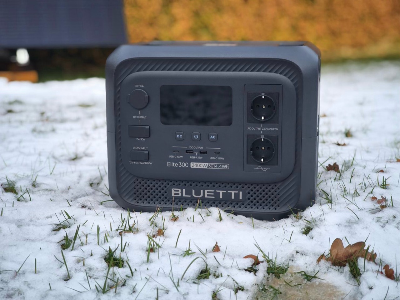 A Bluetti Elite300 portable power station positioned on snowy ground, featuring various output ports and a digital display.