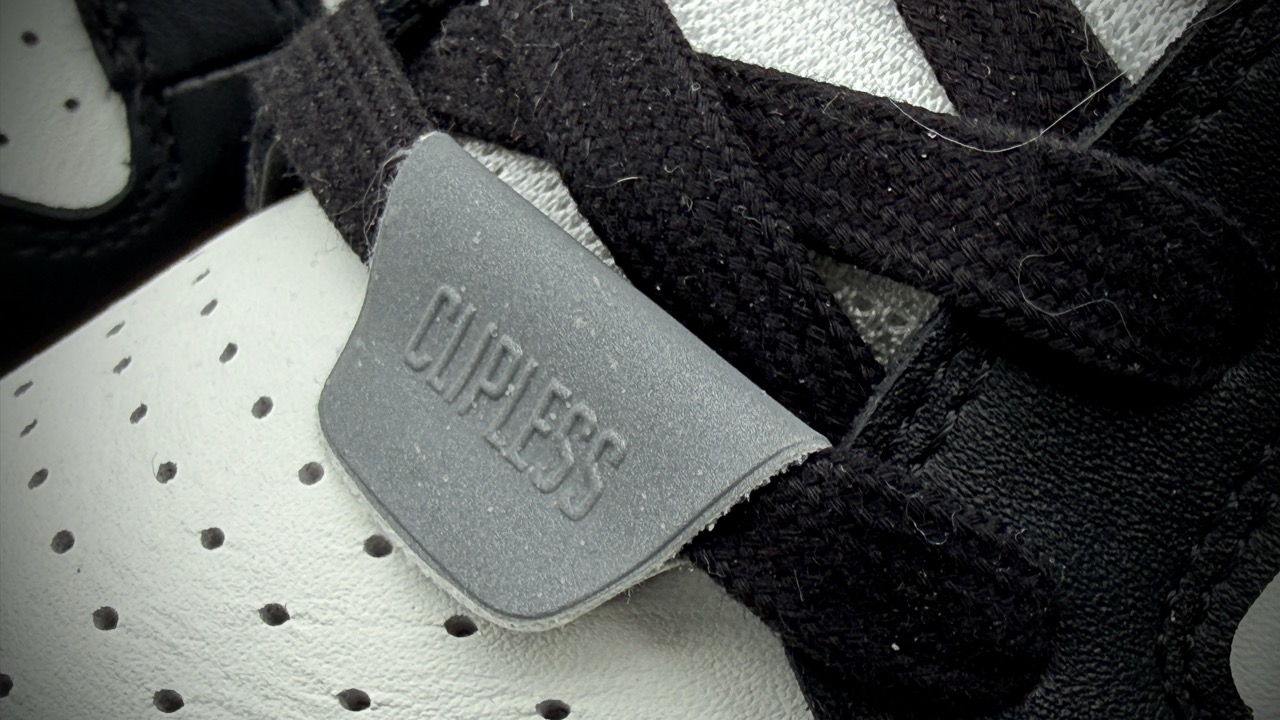 Close-up of a shoe showing a grey Clipless tag and black laces on a white and black sneaker. Drift ARC