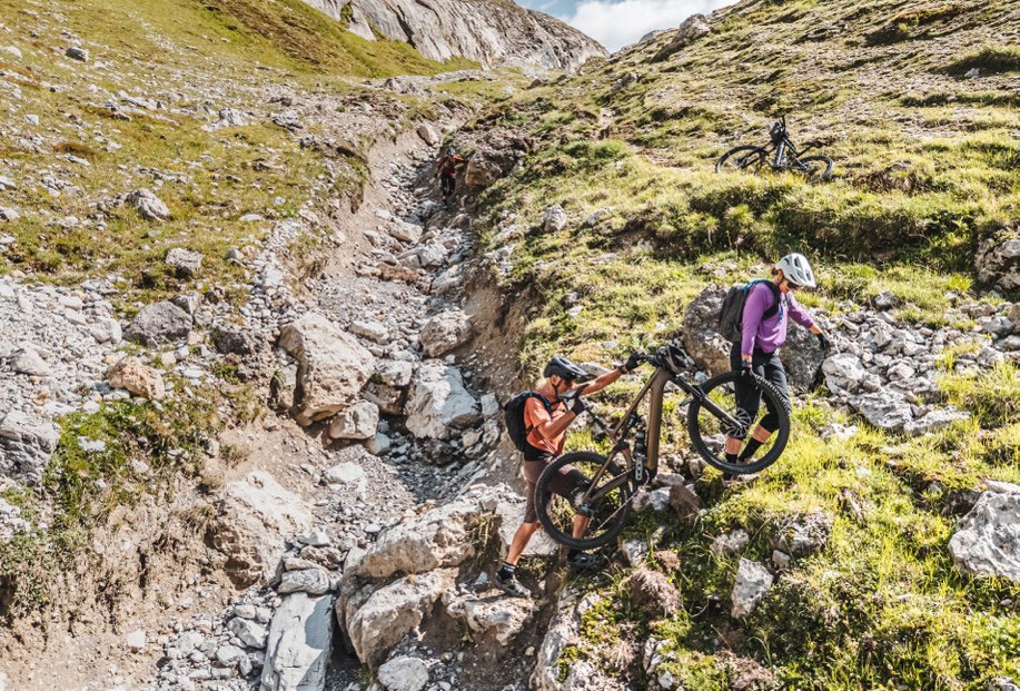 A rider carrying their mountain bike up a steep rocky mountainside.