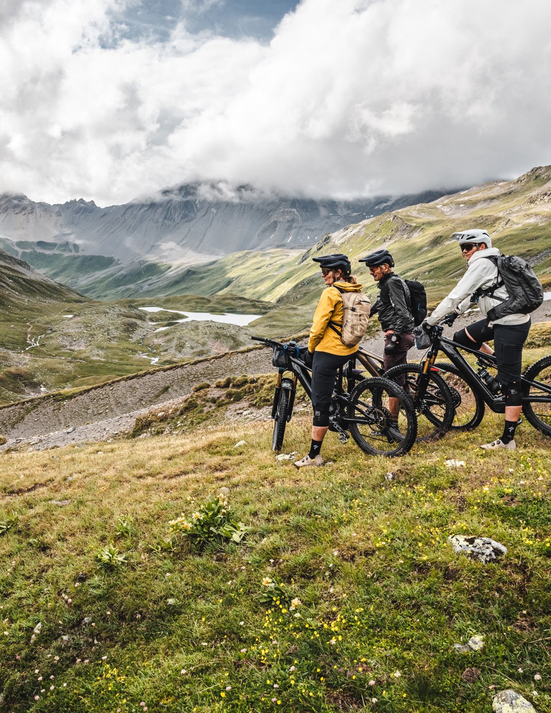 Three riders pausing on a grassy slope, looking out over a misty valley.