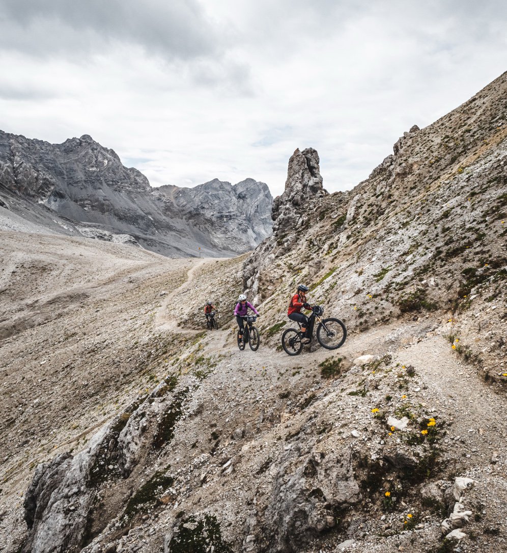 A rider descending a rocky, technical trail among dramatic grey peaks.
