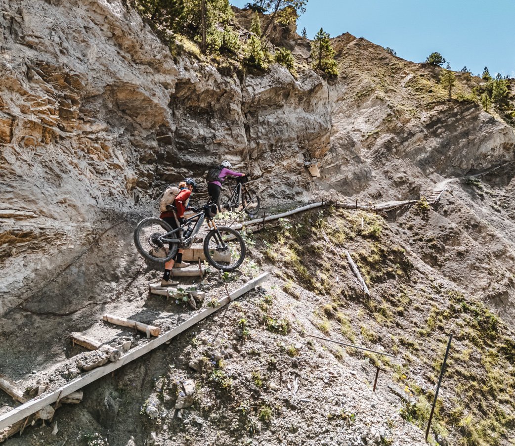 A rider crossing a wooden bridge on a narrow trail over rocky ground.