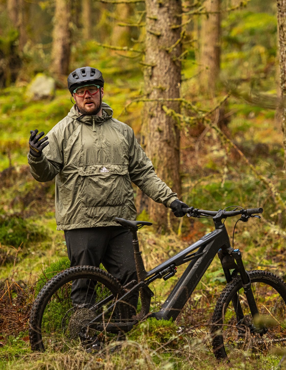 A rider standing with an ebike in a conifer forest.