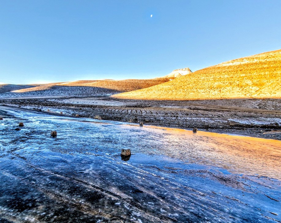 A frozen blue river winding through golden desert hills at dawn.