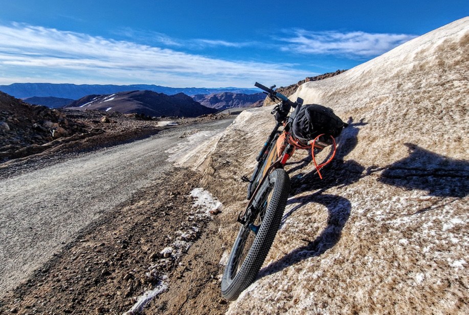 A loaded bike resting on a vast pale scree slope high in the mountains.