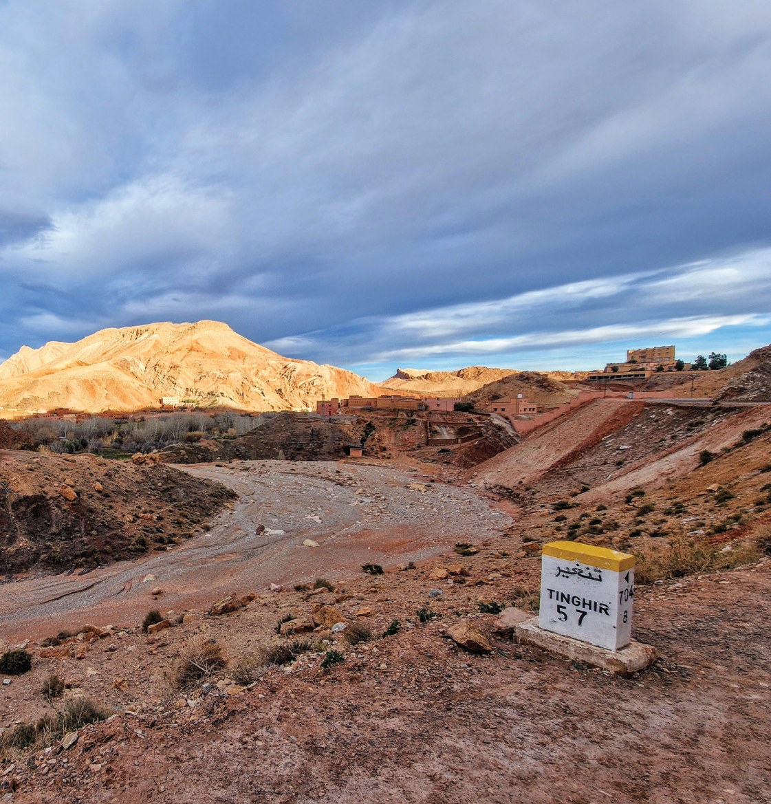 A dirt road descending through red-rock Atlas foothills under cloud.